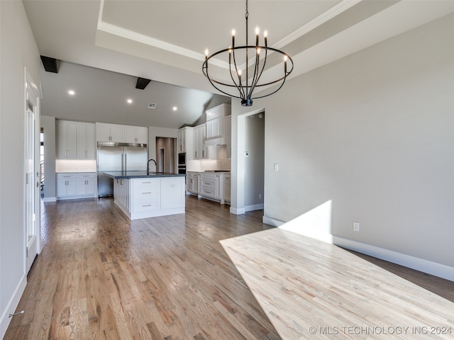 kitchen featuring white cabinetry, stainless steel built in refrigerator, a notable chandelier, light hardwood / wood-style floors, and a kitchen island with sink