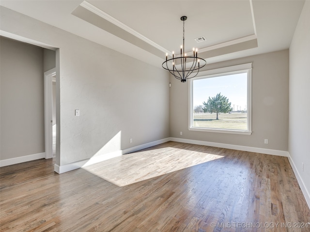 spare room featuring light hardwood / wood-style floors, a raised ceiling, ornamental molding, and an inviting chandelier