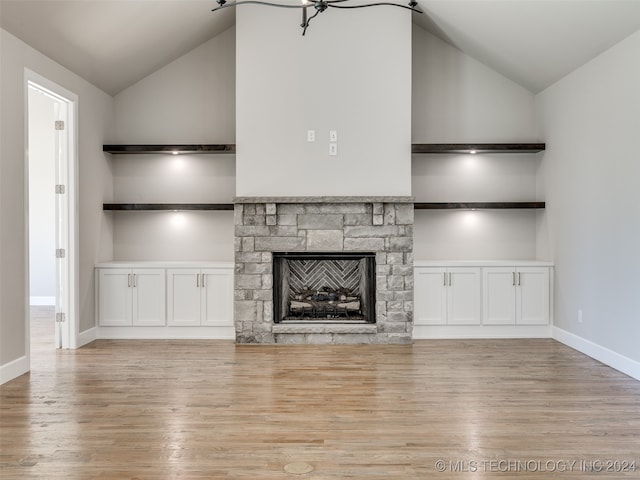 unfurnished living room featuring built in shelves, a stone fireplace, high vaulted ceiling, a notable chandelier, and light wood-type flooring