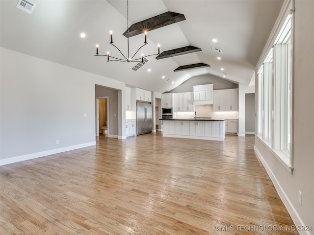 unfurnished living room featuring lofted ceiling with beams, an inviting chandelier, sink, and light hardwood / wood-style flooring