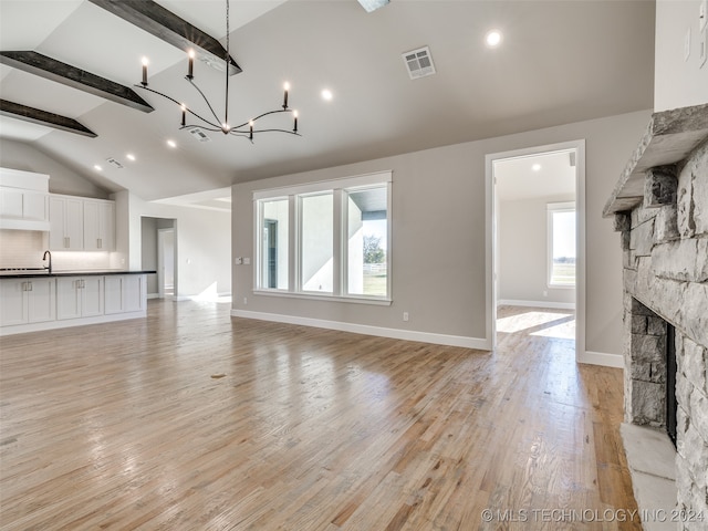 unfurnished living room featuring a stone fireplace, a wealth of natural light, light hardwood / wood-style flooring, and beamed ceiling