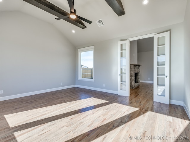 interior space featuring french doors, lofted ceiling with beams, a stone fireplace, ceiling fan, and wood-type flooring