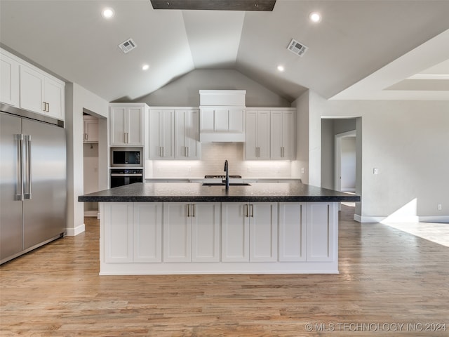 kitchen featuring built in appliances, white cabinetry, a kitchen island with sink, and vaulted ceiling