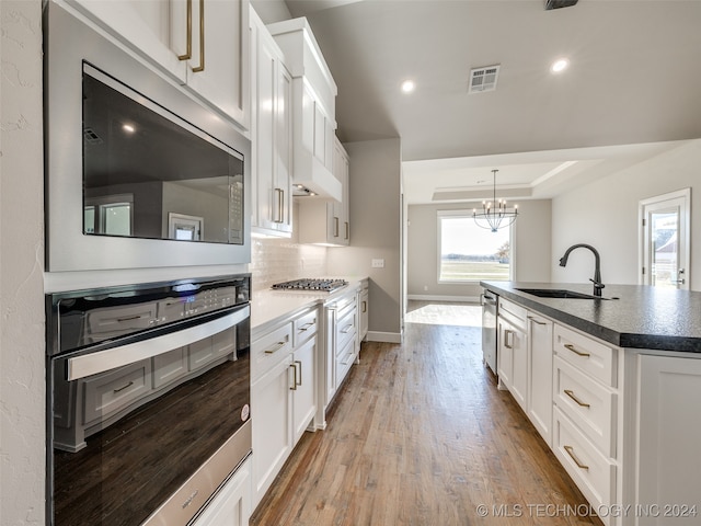 kitchen featuring white cabinets, light wood-type flooring, a chandelier, and sink