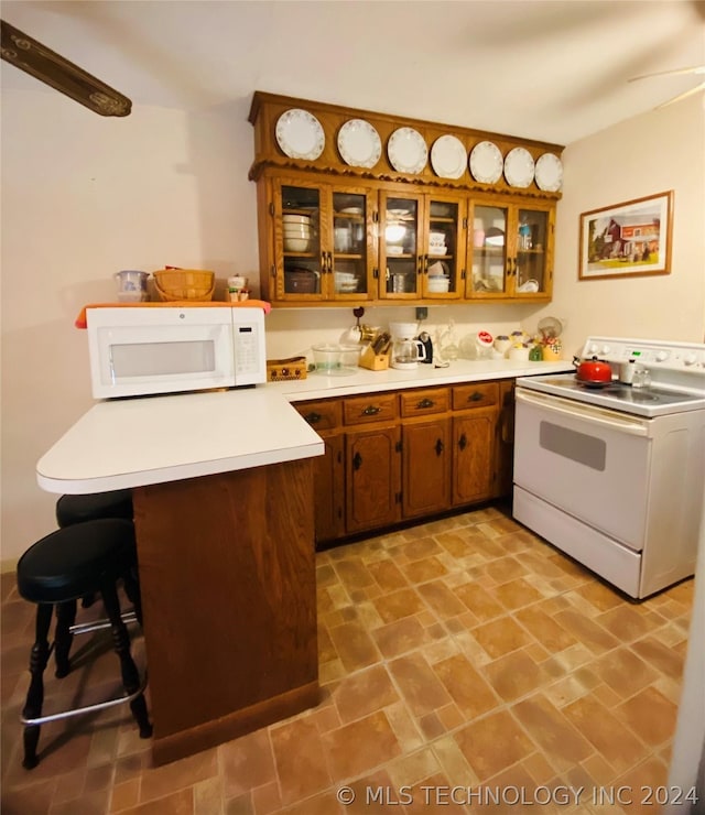 kitchen with a kitchen breakfast bar, ceiling fan, white appliances, and kitchen peninsula