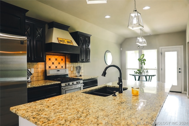 kitchen featuring tasteful backsplash, custom exhaust hood, an island with sink, stainless steel appliances, and sink