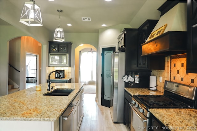 kitchen featuring appliances with stainless steel finishes, premium range hood, tasteful backsplash, and an island with sink