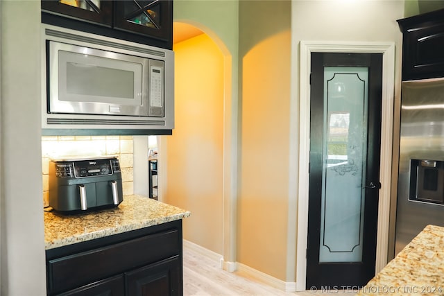 kitchen with backsplash, light stone countertops, light wood-type flooring, and appliances with stainless steel finishes