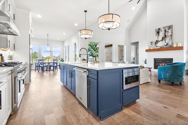 kitchen with white cabinetry, pendant lighting, stainless steel appliances, a center island with sink, and wall chimney exhaust hood