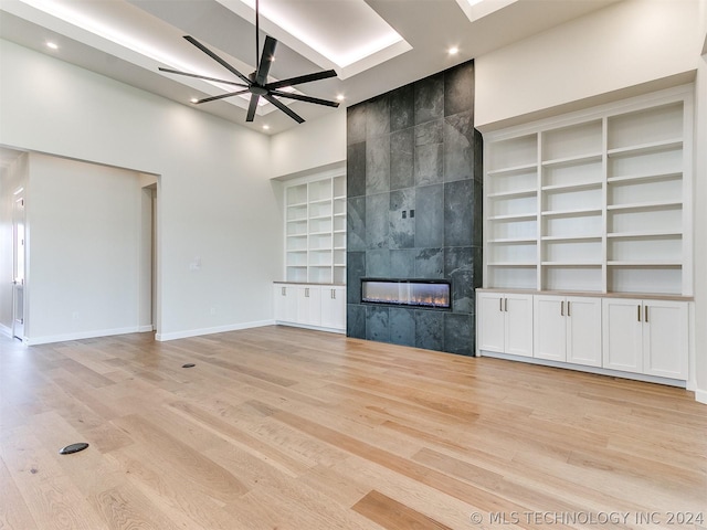 unfurnished living room with a skylight, a tiled fireplace, a high ceiling, ceiling fan, and light hardwood / wood-style flooring