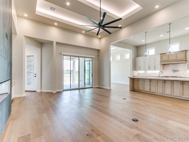 unfurnished living room featuring ceiling fan, a healthy amount of sunlight, light hardwood / wood-style flooring, and a high ceiling