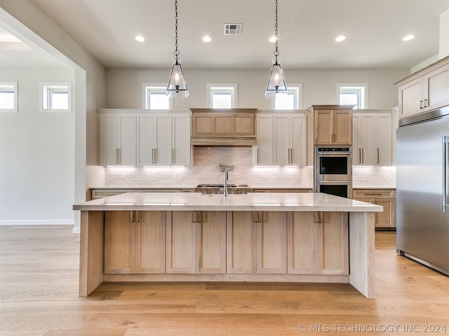 kitchen with stainless steel appliances, light brown cabinetry, and a kitchen island with sink