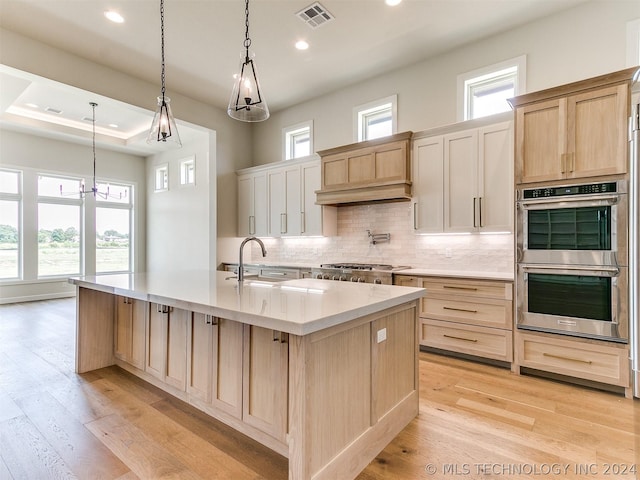 kitchen featuring appliances with stainless steel finishes, decorative light fixtures, sink, and a center island with sink