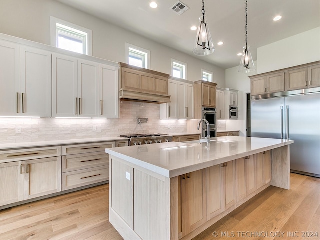 kitchen featuring hanging light fixtures, a center island with sink, light brown cabinets, stainless steel appliances, and decorative backsplash