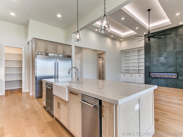 kitchen with sink, hanging light fixtures, a tiled fireplace, a large island with sink, and light brown cabinets