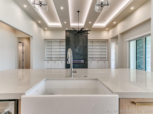 kitchen with light stone counters, a raised ceiling, sink, and light brown cabinets