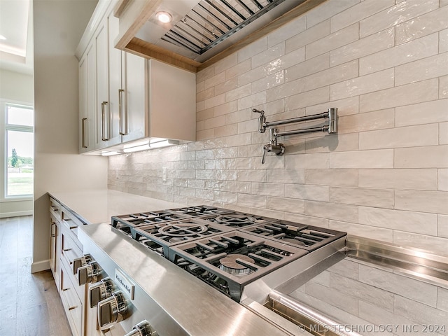 kitchen with light hardwood / wood-style flooring, stainless steel counters, white cabinetry, backsplash, and stainless steel range with gas cooktop