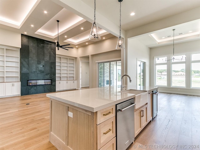 kitchen featuring dishwasher, a kitchen island with sink, built in shelves, decorative light fixtures, and light brown cabinets