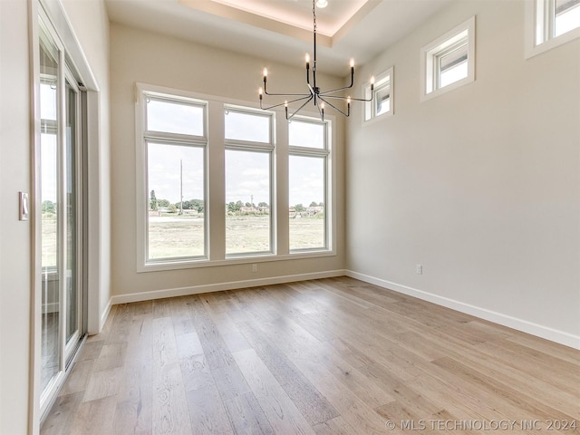 interior space featuring an inviting chandelier, a tray ceiling, and light hardwood / wood-style flooring