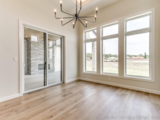 spare room with a healthy amount of sunlight, an inviting chandelier, and light hardwood / wood-style floors