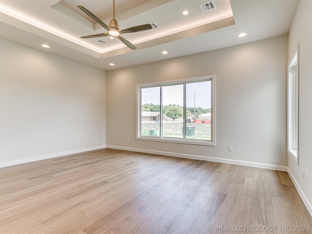 spare room featuring ceiling fan, a tray ceiling, and light hardwood / wood-style floors