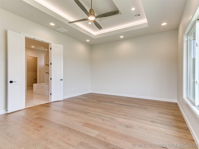 empty room with a tray ceiling, ceiling fan, and light wood-type flooring