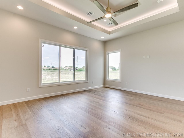 empty room featuring ceiling fan, light hardwood / wood-style floors, and a tray ceiling