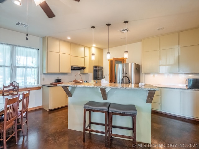 kitchen with light stone countertops, tasteful backsplash, black appliances, decorative light fixtures, and a center island with sink