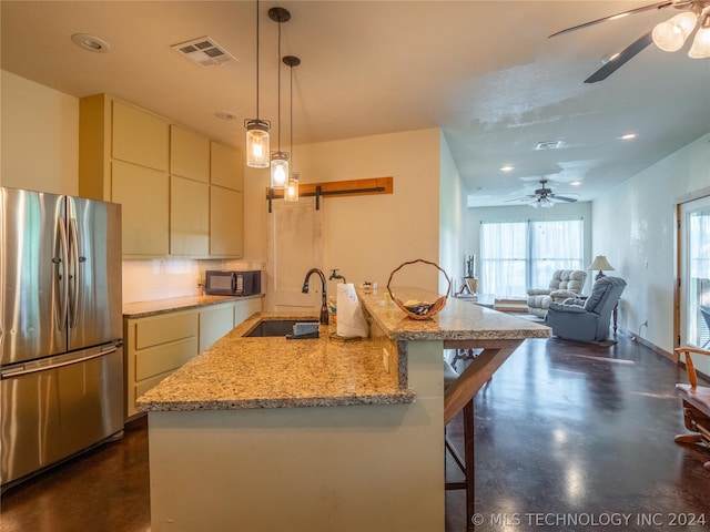 kitchen with hanging light fixtures, stainless steel fridge, sink, and a kitchen island with sink