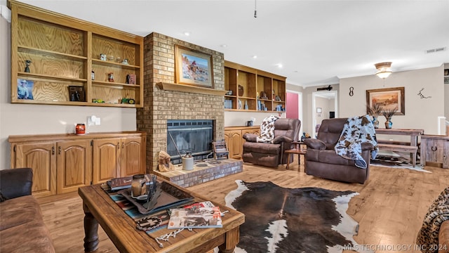 living room with a fireplace, built in features, ornamental molding, and light hardwood / wood-style flooring