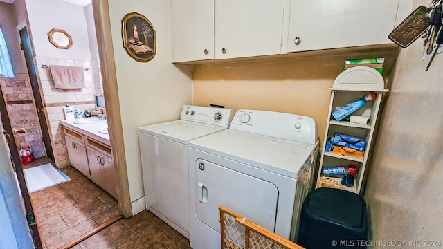 washroom with dark tile patterned flooring, cabinets, sink, and washing machine and clothes dryer