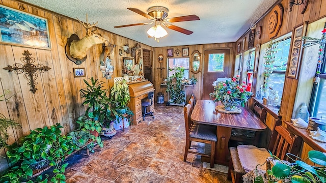 dining area with ceiling fan, a textured ceiling, and wooden walls