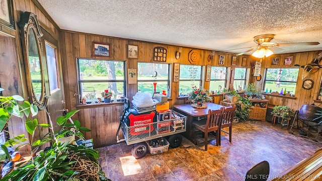 dining space with a wealth of natural light, wooden walls, ceiling fan, and a textured ceiling