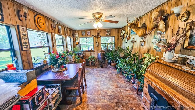 dining room with a textured ceiling, ceiling fan, and wooden walls