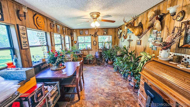 dining room with wood walls, ceiling fan, and a textured ceiling