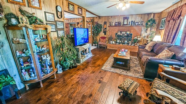 living room featuring dark hardwood / wood-style floors, wood walls, a textured ceiling, and ceiling fan