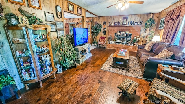 living room with a textured ceiling, ceiling fan, wood finished floors, and a wood stove