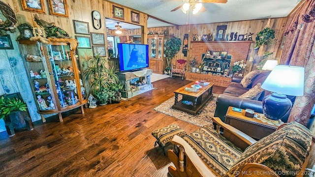 living room featuring ceiling fan, wooden walls, a textured ceiling, and wood finished floors