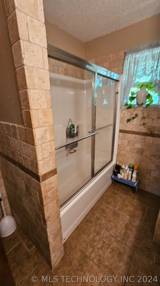 bathroom with combined bath / shower with glass door and a textured ceiling