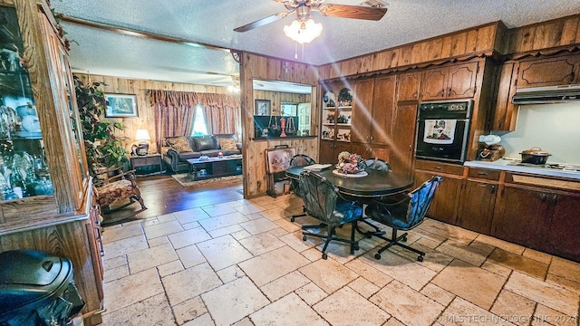 dining room with a textured ceiling, ceiling fan, stone tile flooring, and wooden walls