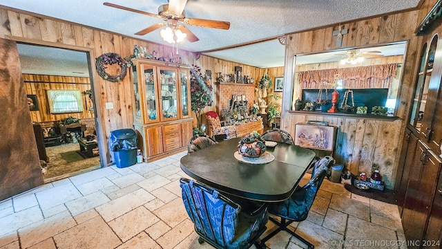 dining area featuring a textured ceiling, wood walls, stone tile flooring, and a ceiling fan