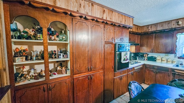 kitchen with a textured ceiling, black oven, brown cabinetry, and light countertops