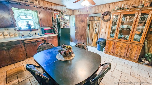 dining room featuring wood walls, ceiling fan, a textured ceiling, and stone tile flooring