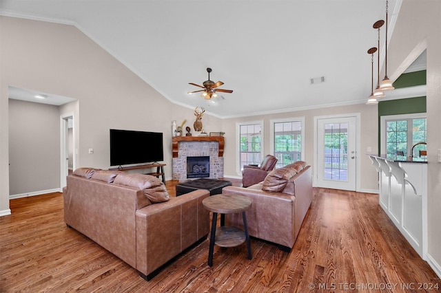 living room featuring light wood-type flooring, ceiling fan, crown molding, a stone fireplace, and lofted ceiling