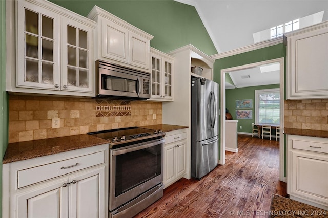 kitchen with backsplash, dark stone counters, stainless steel appliances, vaulted ceiling, and white cabinets