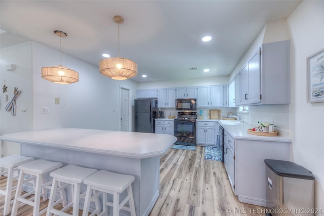 kitchen with decorative light fixtures, black appliances, sink, light hardwood / wood-style flooring, and a kitchen breakfast bar