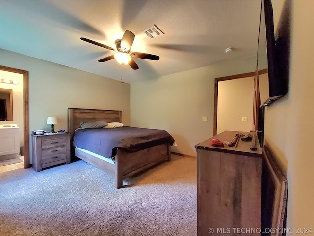 bedroom featuring ceiling fan, light colored carpet, and ensuite bath