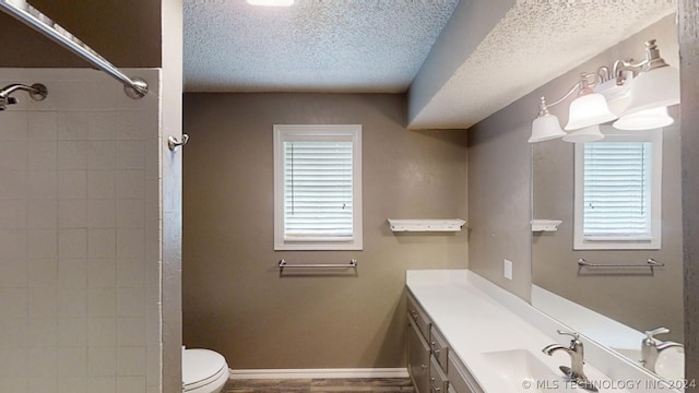 bathroom featuring vanity, toilet, a textured ceiling, and tiled shower