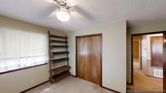 unfurnished bedroom with light carpet, ceiling fan, a closet, and a textured ceiling