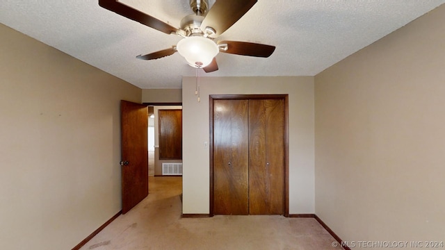 unfurnished bedroom featuring ceiling fan, light carpet, a textured ceiling, and a closet